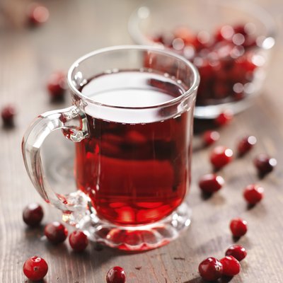 A glass cup of cranberry juice and cranberries on a wooden table