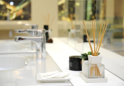 A close-up of wooden sticks in a perfume diffuser near a bathroom sink.