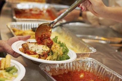 A woman scoops some meatballs onto a friend's plate at a party.
