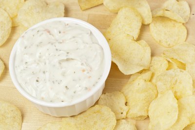 Potato chips around a bowl of french onion dip on a cutting board.