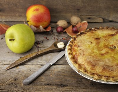 Homemade apple pie on a wooden table with fresh apples on the side