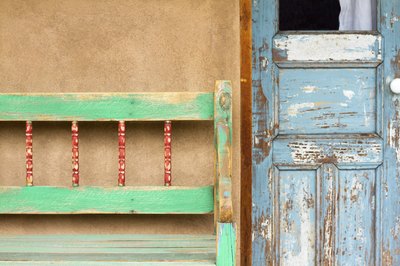 A weathered bench next to the front door of an adobe home.