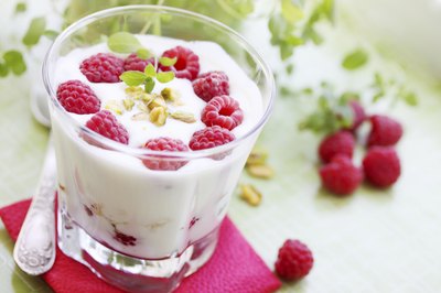 A small glass filled with yogurt and fresh raspberries.