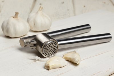 Garlic press with garlic cloves and bulbs.