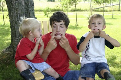 An older brother plays with his young siblings outside.