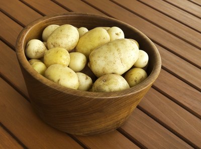 A wooden bowl of golden yukon potatoes on a patio deck.