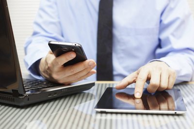 Businessman on smart phone, tablet and laptop in office.