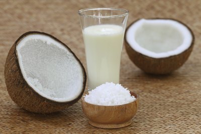 Glass of coconut milk beside halved coconut and shaved coconut.