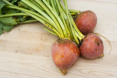 Three whole golden beets with tops on a cutting board.