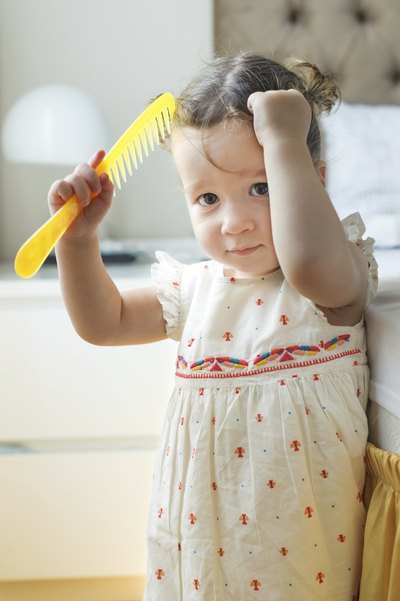 A toddler combs her hair.