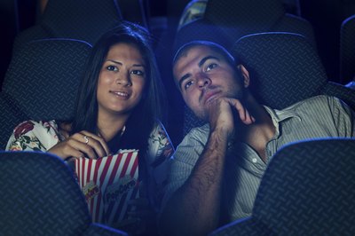 A couple eating popcorn and watching a scary movie at the theater.