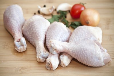 Raw chicken legs wtih vegetables on a cutting board.