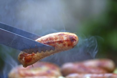 Thongs holding pork sausage.