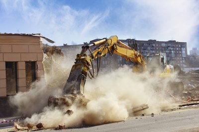 An excavator destroys a builidings wall.