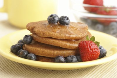 A stack of whole-wheat pancakes with blueberries and a strawberry.