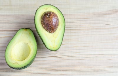Halved avocado with a pit on a wood surface.