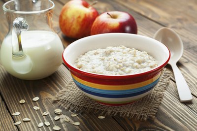 A bowl of oatmeal next to a pitcher of milk and some apples.