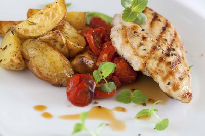 Seasoned chicken and potatoes with tomatos on a plate.