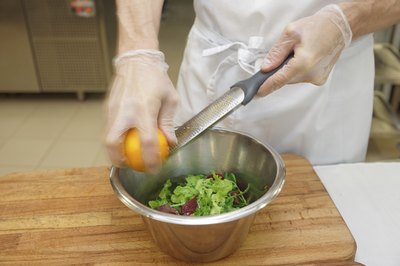 A chef wears gloves and an apron while zesting a lemon.