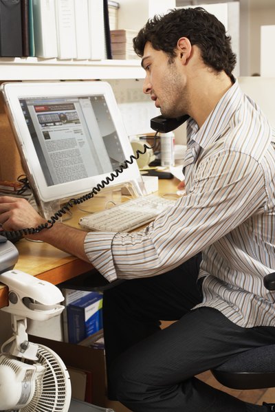 A man looks at his computer screen while talking on the phone.