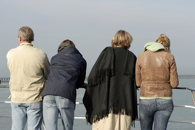 The backs of four cruise ship passengers looking over a rail.