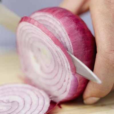 A woman slices a red onion.