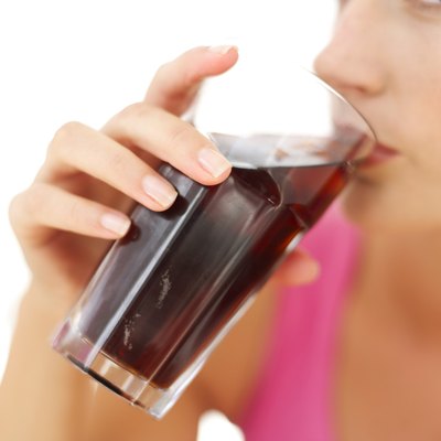 A woman drinks a glass of cola.