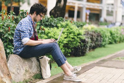 A young man perusing social media sites on his laptop in a courtyard.