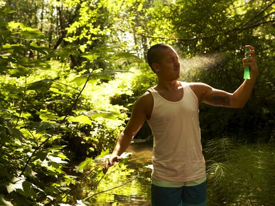A man sprays insect repellant on his face.