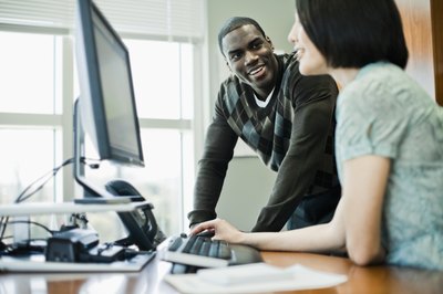 A man works with a woman at an office work station.