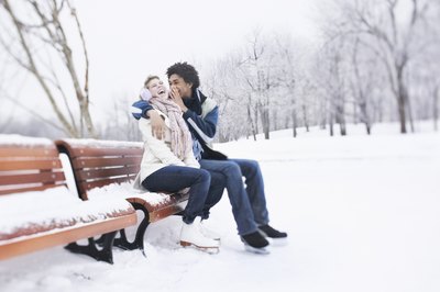 A couple is sitting on a park bench wearing ice skates.
