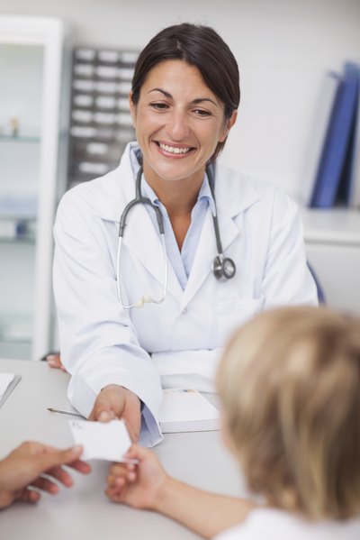 A pediatrician hands a prescription to a mother and child.