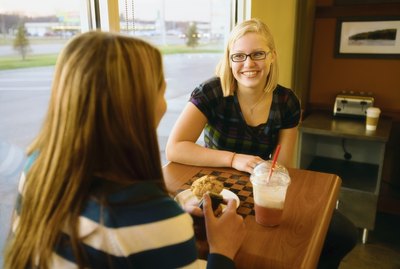 Two women sit at a checkerboard table in a coffeehouse.