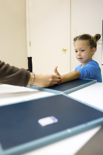 A physician places a girl's arm on an xray pad.