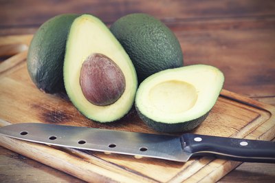 Halved avocados on a cutting board next to a knife.