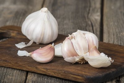 Garlic bulb and cloves on a wood cutting board.