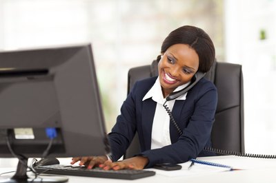 Young business woman on phone with client while researching on the computer.