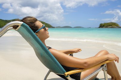 A young woman reclines in a lounge chair on the beach.
