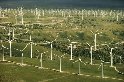 A large number of wind turbines on top of a grassy hill.