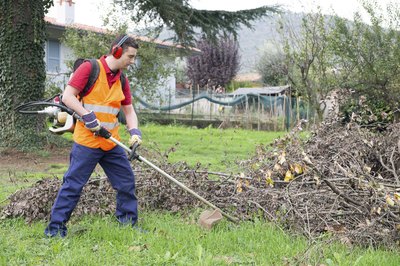 A lawn care worker using a trimmer in the yard.