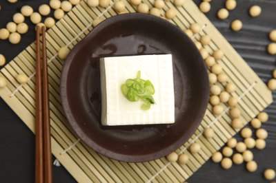 A block of tofu on a plate surrounded by soy beans.