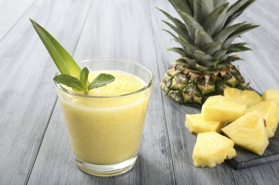 A glass of pineapple juice next to pineapple slices