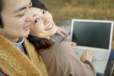 A man embraces a woman while she is looking at a computer.