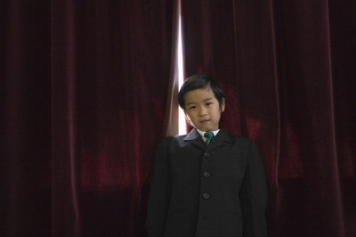 A boy wearing a suit in front of red curtains.