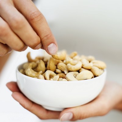 A man eats cashews from a bowl.