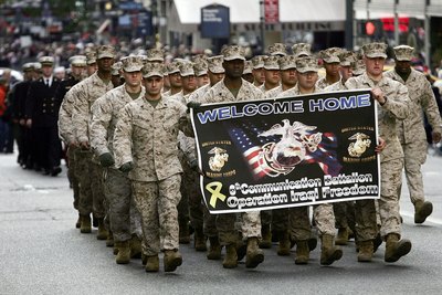 Army veterans marching in a parade holding up a banner
