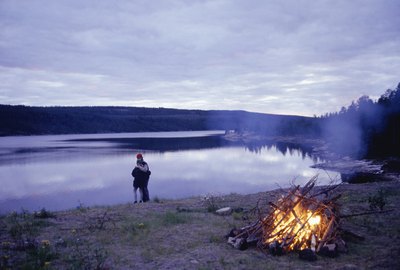 a couple standing on the shore with a campfire in the foreground.
