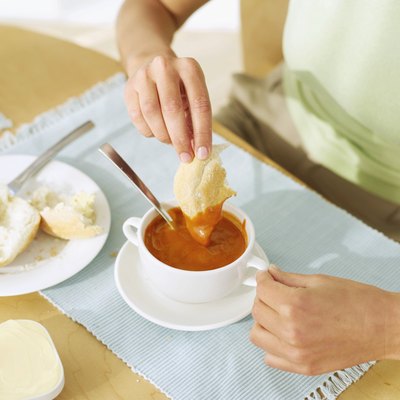 A person is dipping bread into tomato soup.