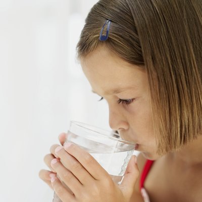 A young girl drink water while feeling ill.