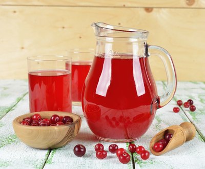 Pitcher and glasses filled with cranberry juice as well as a bowl of cranberries on a table